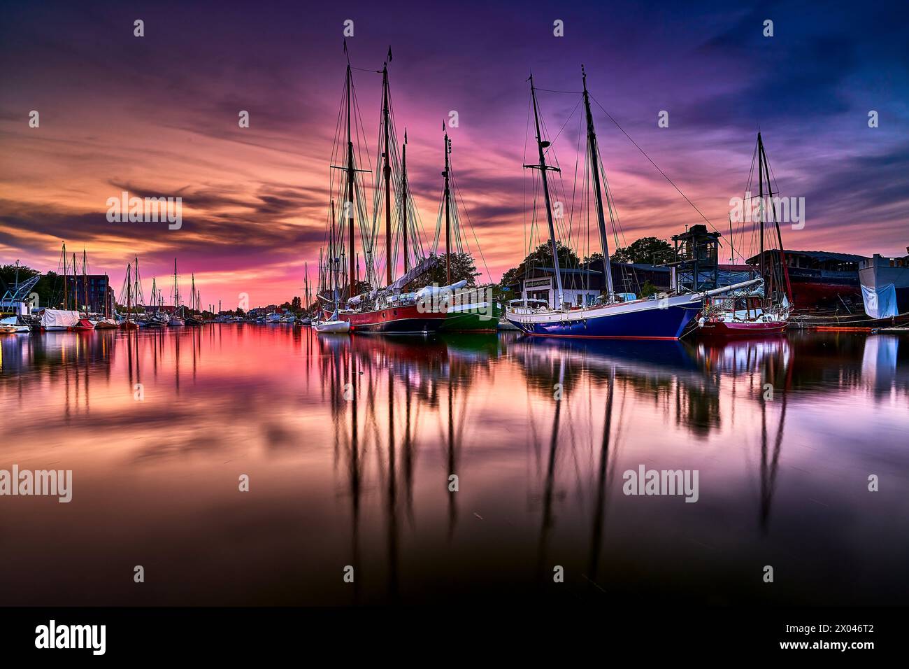 Pittoresco scenario in cui le navi riposano nel porto, e la luce serale inonda il cielo di toni caldi. Al centro dell'attenzione c'è il marinaio ormeggiato Foto Stock