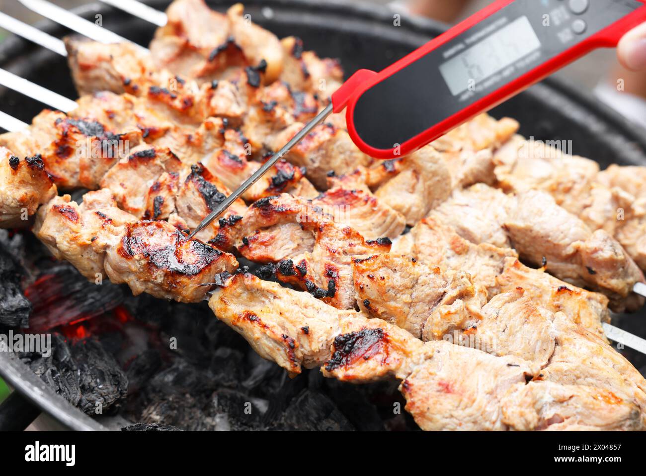Uomo che misura la temperatura del delizioso kebab su braciere in metallo, primo piano Foto Stock