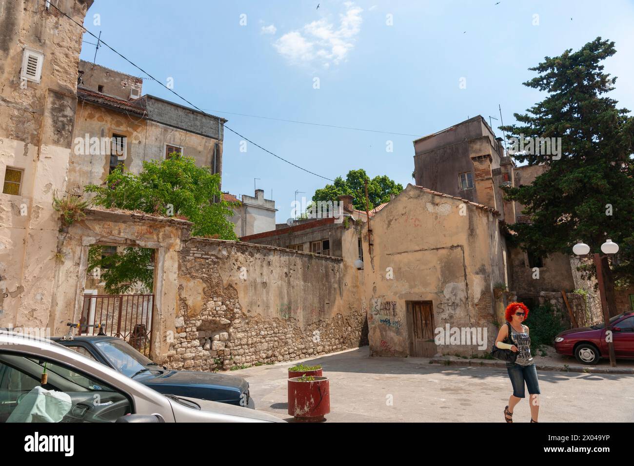 Zara Croazia - maggio 26 2011; donna con i capelli rossi cammina dall'altra parte della strada circondata da vecchi edifici. Foto Stock