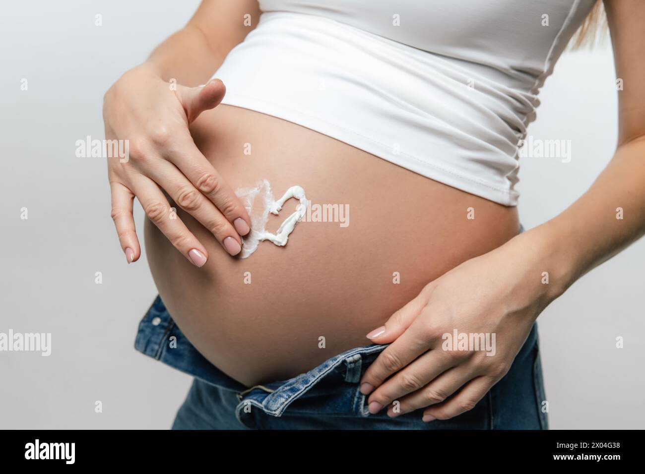 Donna incinta che applica crema idratante nella sua pancia grande Foto Stock