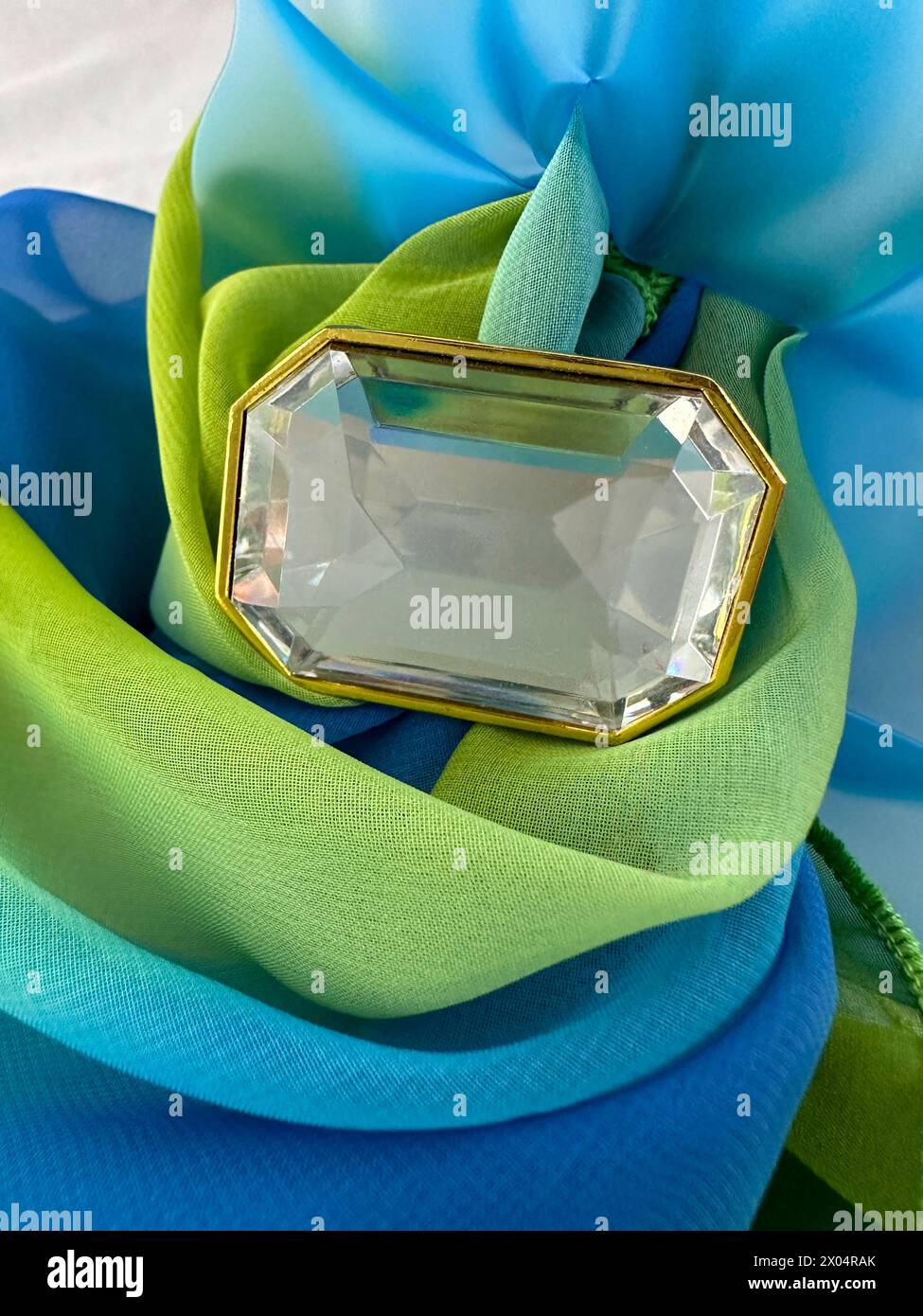 La spilla in pietra strass è circondata da un tessuto verde blu. Il perno in vetro con cornice dorata può contenere un messaggio di testo. Il tessuto è trasparente con spilla vintage. Foto Stock