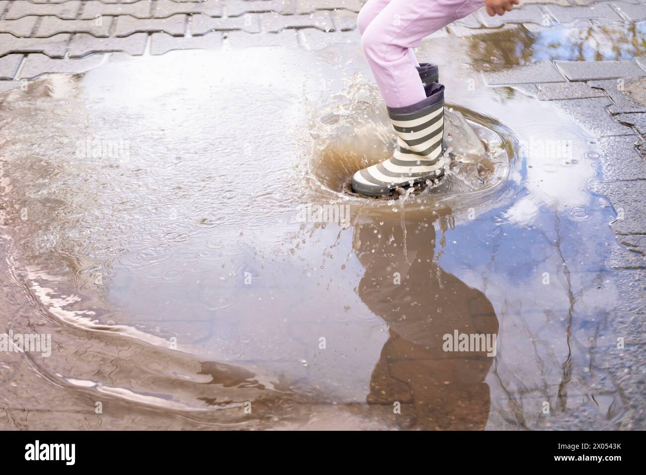 la maliziosa ragazza di 5 anni con stivali di gomma salta con gioia in pozzetto, ravvicinare i piedi dei bambini in spruzzi d'acqua, , catturando gioie pure e semplici chi Foto Stock