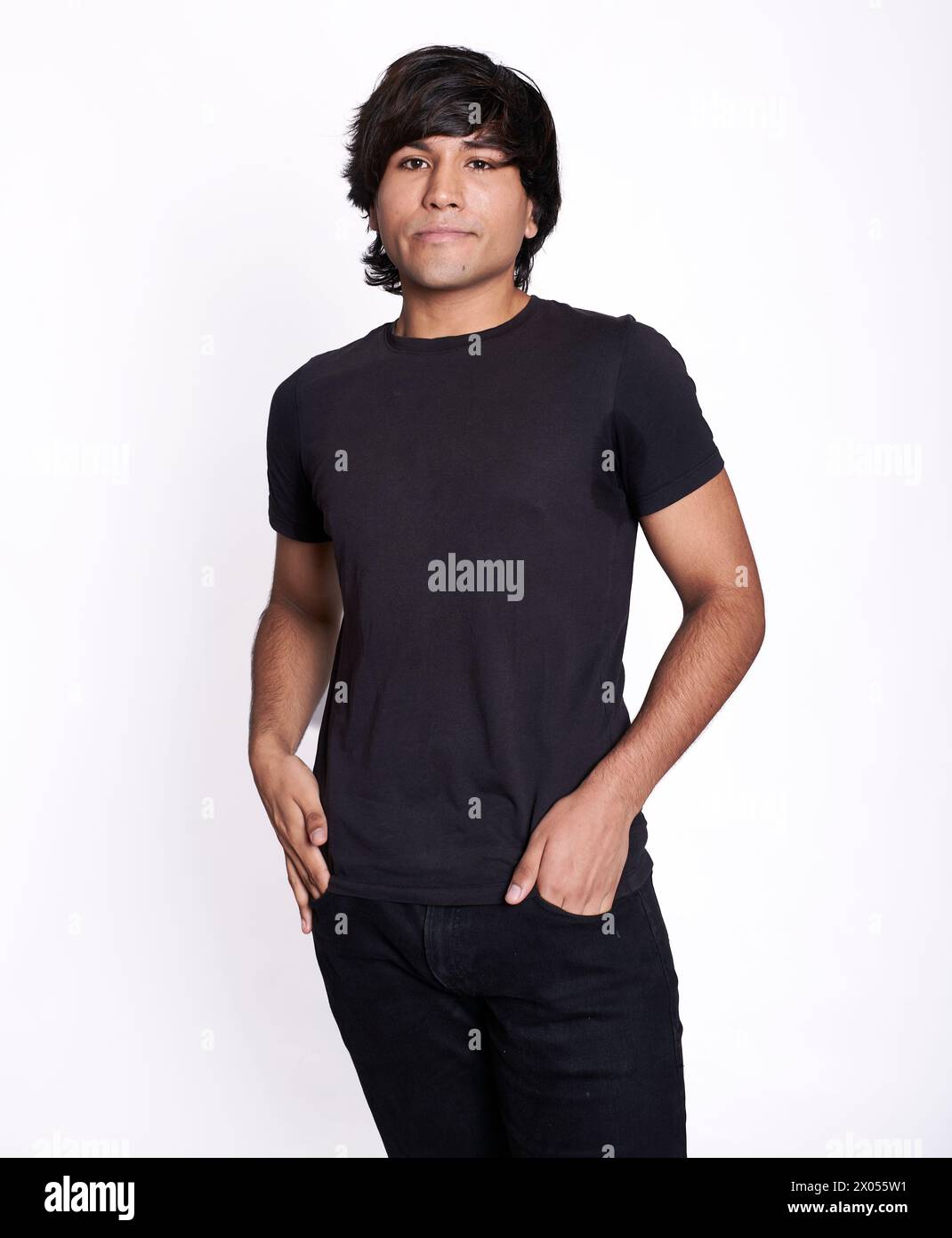 Foto americana di un giovane latino con entrambe le mani nella tasca dei suoi jeans neri. Lo sfondo è bianco Foto Stock