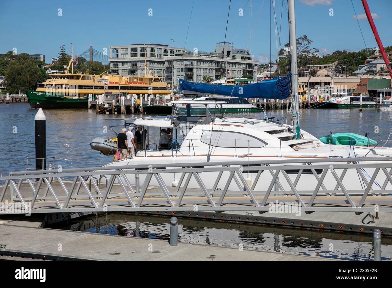 Catamarano a vela con persone che si imbarcano dal pontile a Mort Bay Sydney con il cantiere Balmain sullo sfondo, NSW, Australia Foto Stock