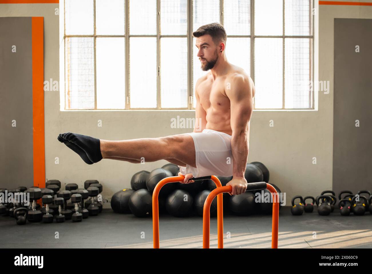 Vista laterale del muscolo maschile che fa L siedono su barre parallele esercizi di calistenica nel moderno fitness club Foto Stock