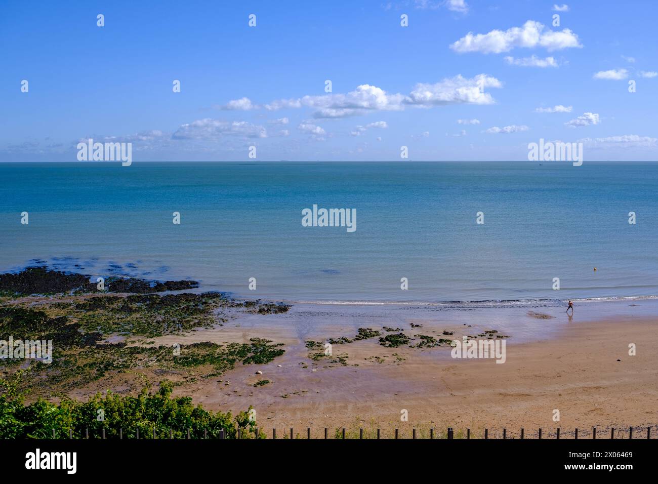 Oceano calmo, cielo blu con soffici nuvole bianche, spiaggia sabbiosa con qualche vegetazione sulla sinistra a Thanet Coast Kent, Inghilterra, Regno Unito. Foto Stock