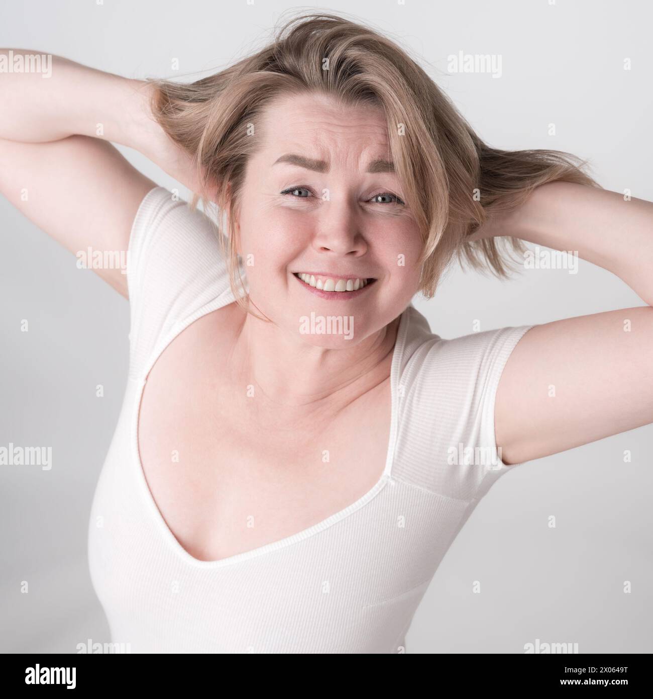 Ritratto di donna adulta matura con le mani dietro la testa e il sorriso. Una donna felice indossa un costume. La ripresa ad angolo alto cattura perfettamente il wom biondo Foto Stock