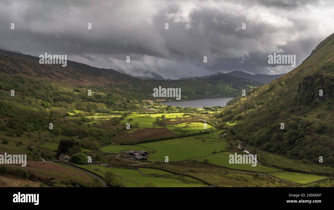 Le nuvole di Moody si stagliano su una lussureggiante valle verde, circondata dalle montagne di Snowdonia, Galles del nord, Regno Unito, con il sole che mette in risalto parti del vallone Foto Stock