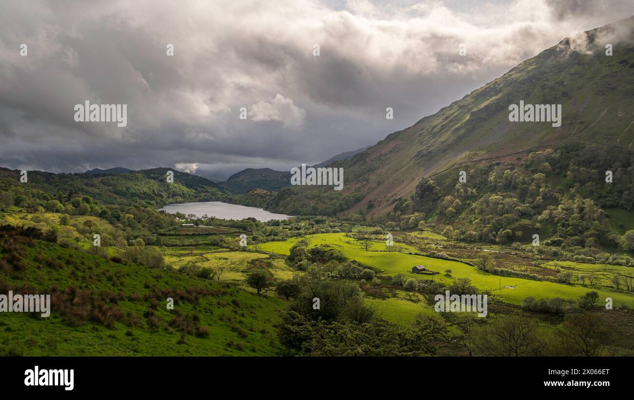 Le nuvole di Moody si stagliano su una lussureggiante valle verde, circondata dalle montagne di Snowdonia, Galles del nord, Regno Unito, con il sole che mette in risalto parti del vallone Foto Stock