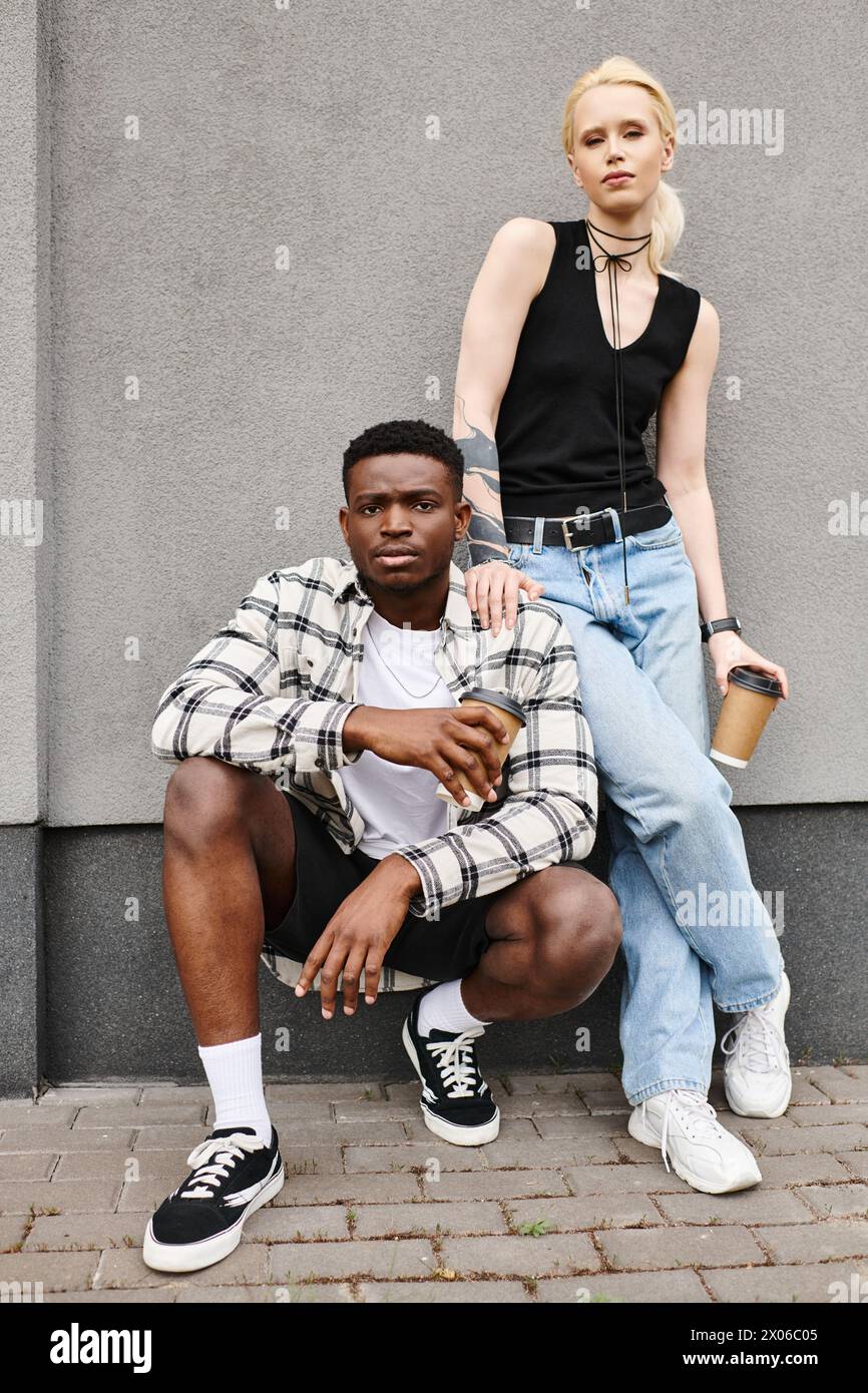 Una coppia felice, un uomo e una donna di origini diverse, posano insieme in una strada urbana vicino a un edificio grigio. Foto Stock