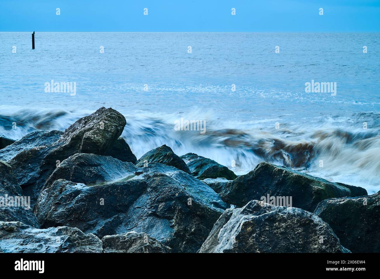 Massi di granito scuri contro le onde che si infrangono Foto Stock