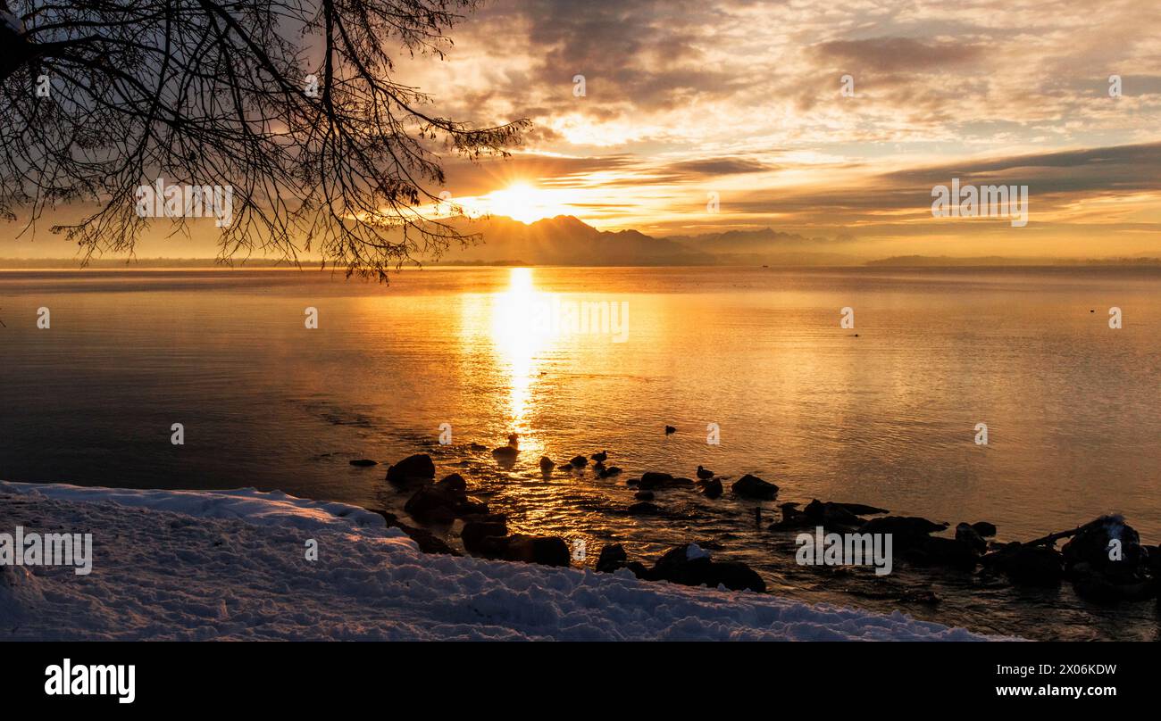 La luce dorata del sole invernale che tramonta sul panorama alpino si riflette sul lago, la Germania, la Baviera e il lago Chiemsee Foto Stock