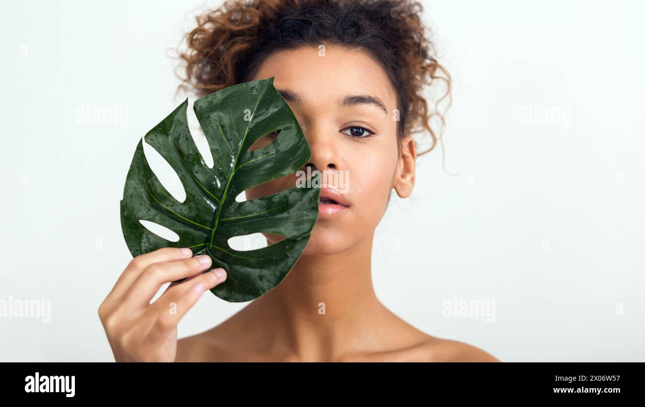 Donna con foglie tropicali che coprono metà del viso Foto Stock