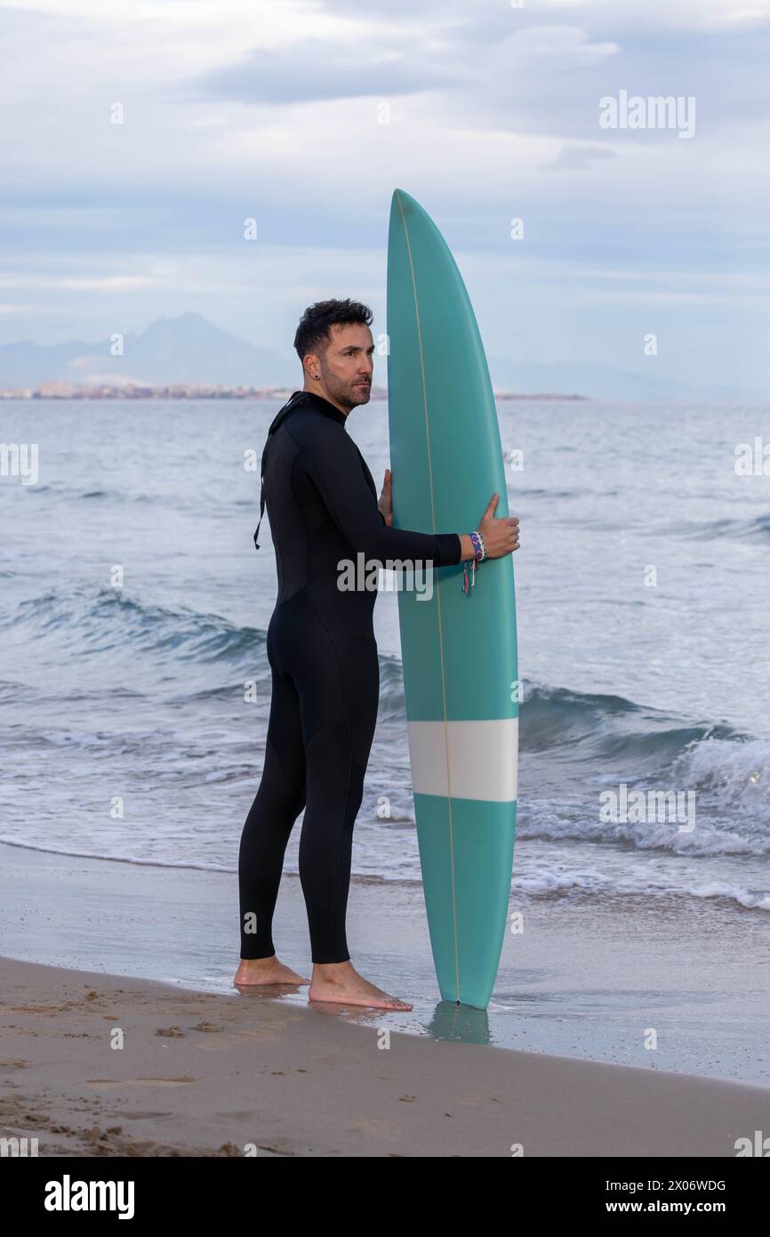 Surfista con muta e tavola da surf sulla spiaggia Foto Stock