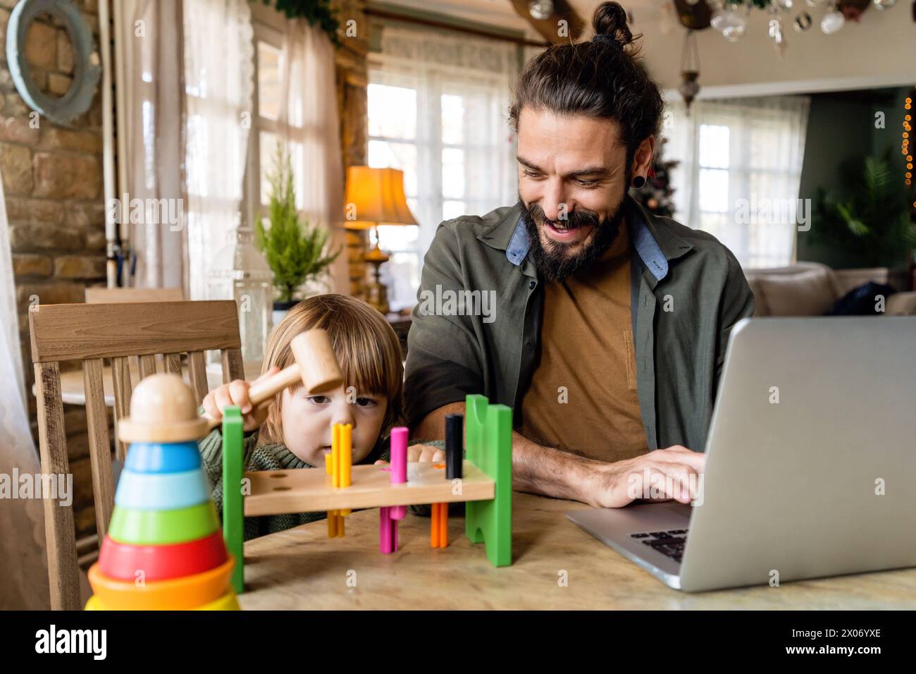 Concetto di freelance e paternità multitasking. Padre single che lavora con un bambino e un computer portatile Foto Stock