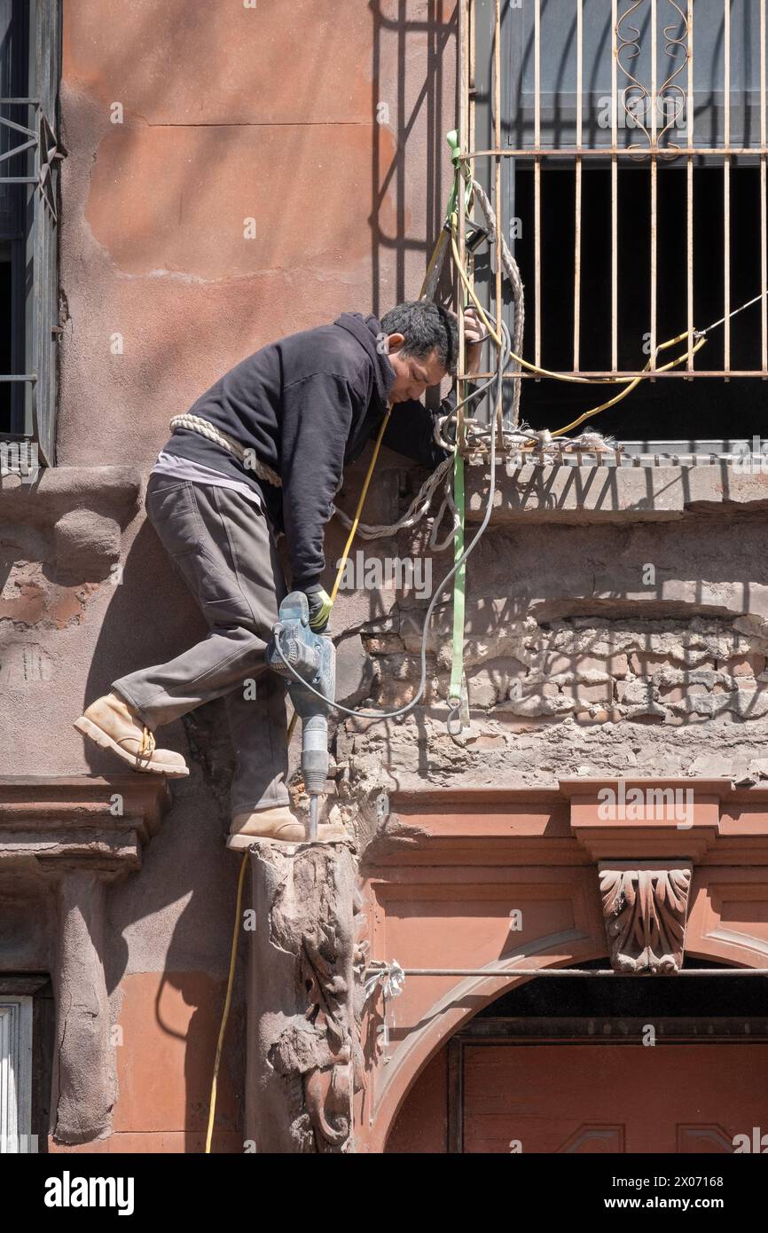 Un operaio edile in una posizione precaria rompe il cemento con il martello. Una ristrutturazione di una vecchia casa in Bedford Ave a Williamsburg, New York. Foto Stock