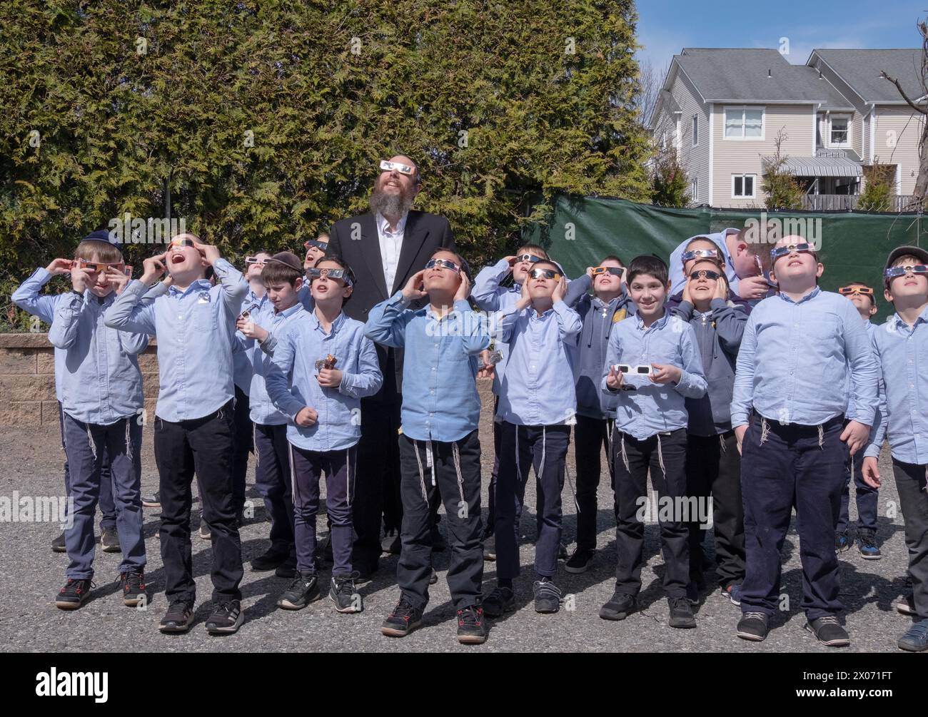 Gli studenti ebrei della yeshivah e i loro insegnanti rabbini guardano l'eclissi solare del 2024 dal loro cortile di scuola nella contea di Rockland, New York. Foto Stock