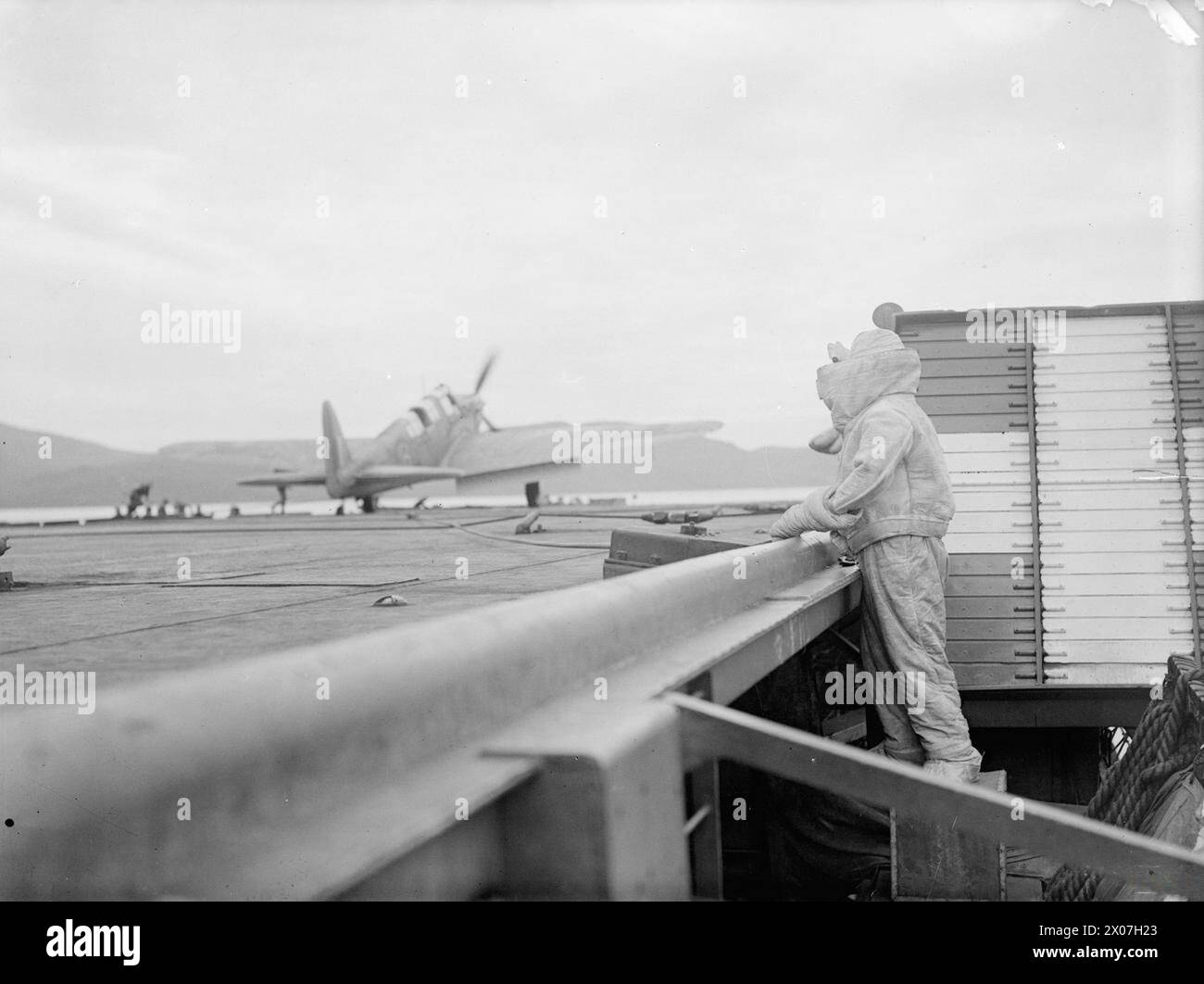 Dal 15 al 17 agosto 1943, la HMS Argus al largo di Lamlash addestrò i piloti della Fleet Air Arm negli sbarchi di portaerei, in occasione del suo 25° anniversario. Un membro del gruppo dei vigili del fuoco in abiti di amianto ha osservato un atterraggio di Hawker Hurricane. Foto Stock