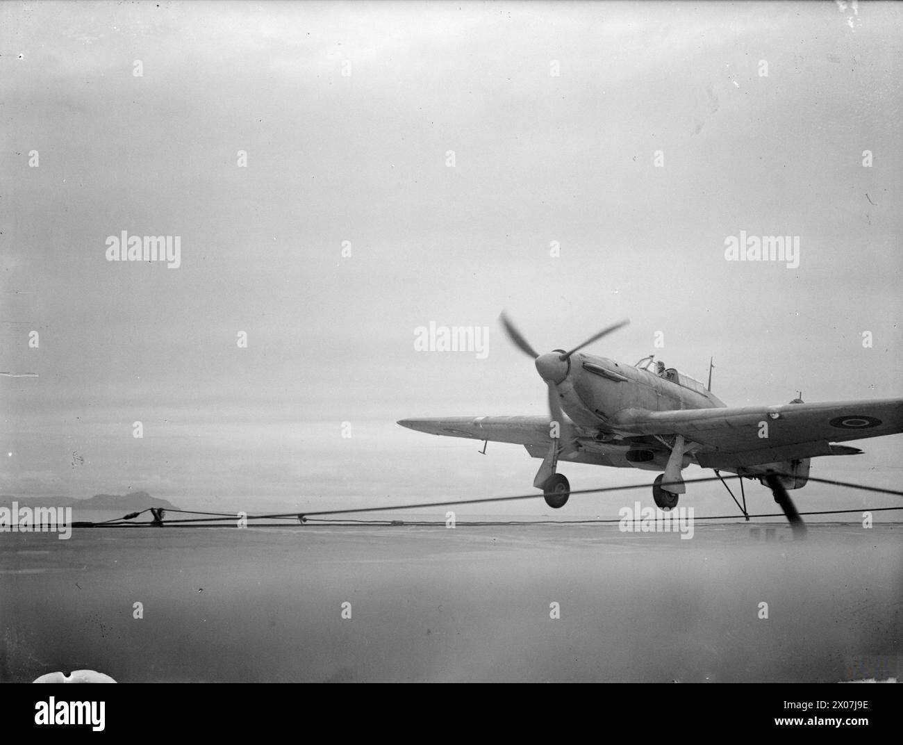 Tra il 15 e il 17 agosto 1943, la HMS Argus al largo di Lamlash addestrò i piloti della Fleet Air Arm negli sbarchi di portaerei, celebrando 25 anni di servizio. Un Hawker Sea Hurricane viene mostrato atterrare usando il gancio di arresto. Foto Stock