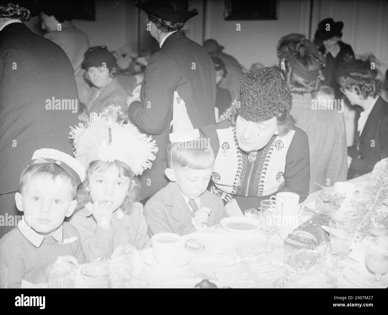 FESTA DI NATALE DELL'AMMIRAGLIATO PER I FIGLI DEGLI UFFICIALI NAVALI ALLEATI. ADMIRALTY HOUSE, 17 DICEMBRE 1942, LA SIGNORA A V ALEXANDER, MOGLIE DEL PRIMO SIGNORE DELL'AMMIRAGLIATO, INTRATTENNE I FIGLI DELLE NAZIONI ALLEATE AD UNA FESTA NATALIZIA ALL'ADMIRALTY HOUSE. TRA GLI OSPITI PRESENTI VI ERANO: WINSTON CHURCHILL, ERNEST BEVIN, MADAME MAISKY, MRS DUNCAN SANDYS, MRS LEE, LA SIGNORA RANDOLPH CHURCHILL, LA SIGNORA ATLEE E MOLTE ALTRE PERSONALITÀ BEN NOTE. - Madame Maisky aiuta tre bambini sovietici al tavolo da tè. La ragazza è Tatiana Narlamof Foto Stock