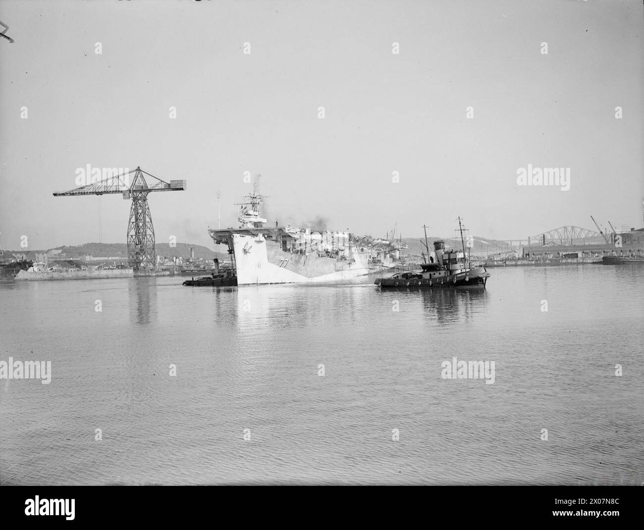 La HMS Nabob, una portaerei di scorta silurata a 1070 miglia dalla sua base, arrivò ai cantieri navali di Rosyth il 18 settembre 1944, assistita dai rimorchiatori mentre entrava nel molo principale. Foto Stock