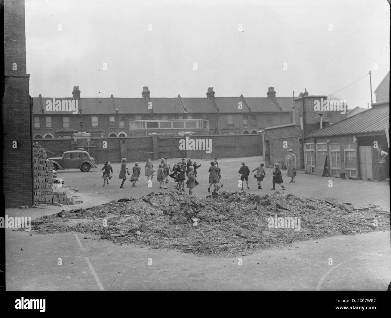 I bambini della Lombard Wall School nel sud-est di Londra giocano nel parco giochi sotto la supervisione di un'insegnante femminile nel 1941. Una grande pila di macerie in primo piano mostra i danni causati da un raid aereo durante la seconda guerra mondiale. Foto Stock