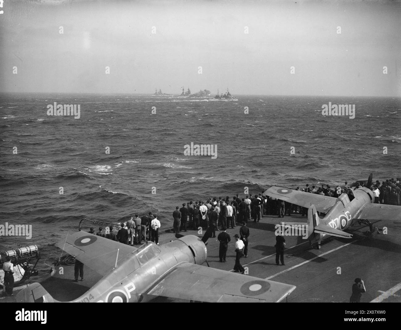 Gli uomini a bordo della HMS Formidable nel Mediterraneo dal 15-17 aprile 1943 osservano i cannoni da 16 pollici della corazzata Rodney sparare, insieme all'incrociatore britannico Newfoundland e alla corazzata Nelson. Foto Stock