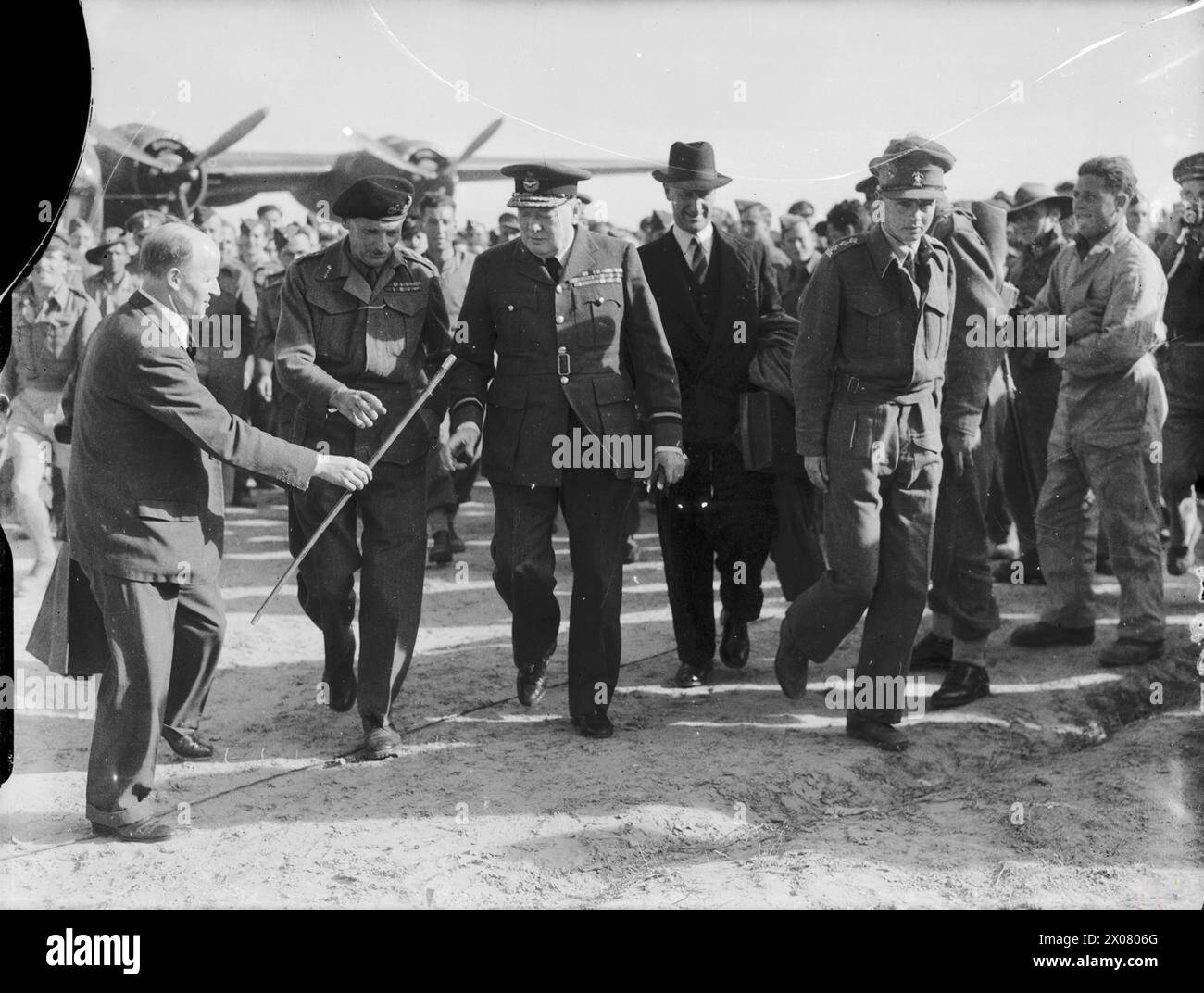 Winston Churchill cammina con il tenente generale Bernard Montgomery e altri in un aeroporto del Nord Africa all'inizio di agosto 1942, usando un bastone come supporto. Foto Stock