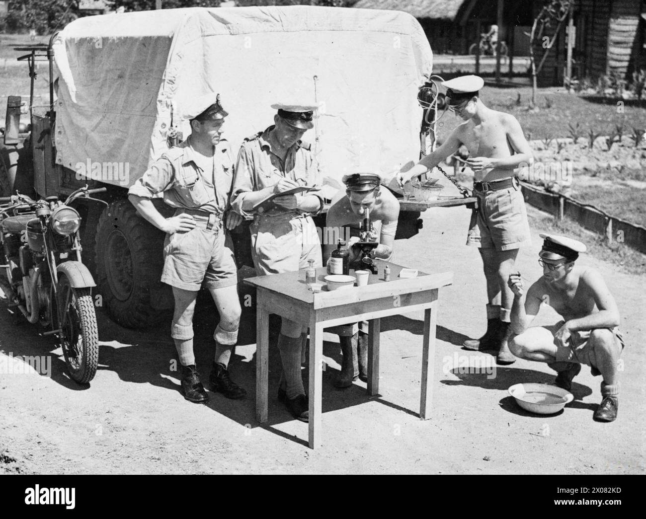 LA ROYAL NAVAL SCHOOL OF MALARIA AND Hygiene CONTROL, NR COLOMBO, CEYLON, DICEMBRE 1944 - l'unità della RN School of malaria and Hygiene Control torna alla sua stazione ed esamina il materiale raccolto dalle paludi della giungla. Sulla destra vengono selezionate larve di zanzara per l'identificazione. Sono colorati (secondi da destra) e montati per l'esame al microscopio. I risultati vengono poi registrati dal medico mentre il sottufficiale guarda alla Royal Navy, HMS Puncher, Patrol Vessel, (1988) Foto Stock