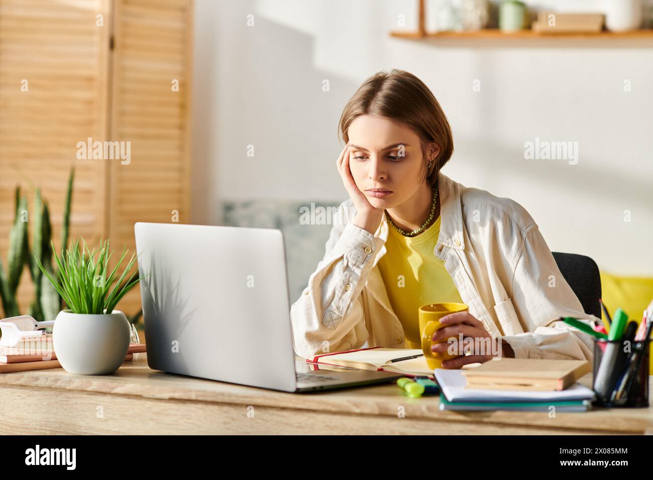 Una teenager concentrata che studia su una scrivania di legno con un laptop aperto di fronte a lei per l'e-learning. Foto Stock