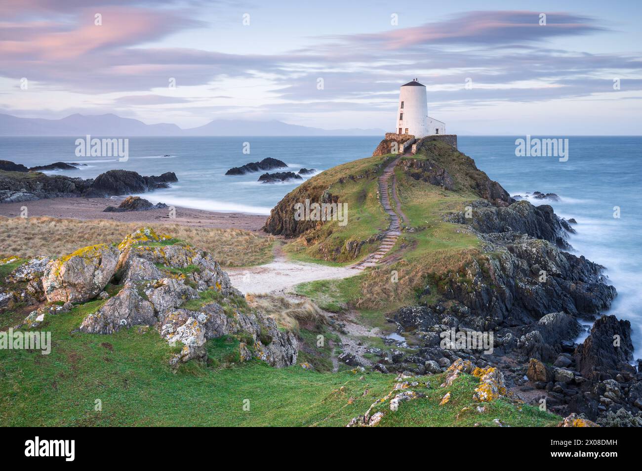 Il faro di TWR Mawr si illumina dolcemente con la luce prima dell'alba durante una mattinata torbida sull'isola di Llanddwyn, Anglesey, Galles del Nord. Foto Stock