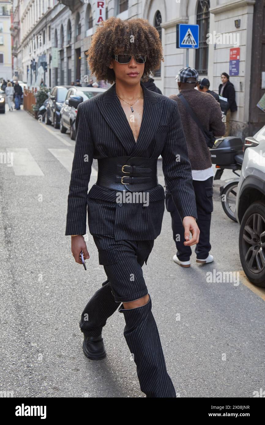 MILANO, ITALIA - 21 FEBBRAIO 2024: Uomo con giacca a righe, pantaloni e cintura in pelle nera prima della sfilata Iceberg, Milano Fashion Week Street Foto Stock
