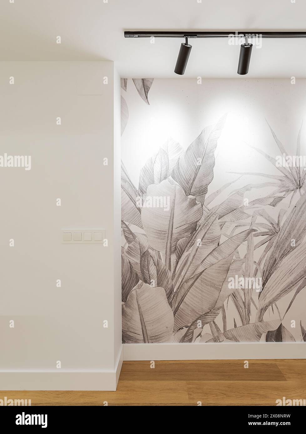 Uno spazio interno contemporaneo caratterizzato da un grande design di carta da parati in foglie tropicali e sistema di illuminazione a binario sospeso, con pavimento in legno che aggiunge calore Foto Stock