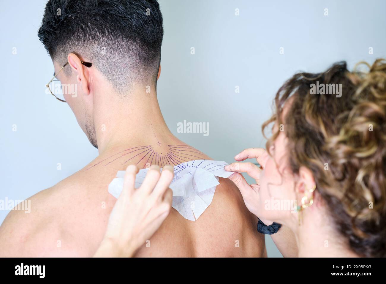 Un tatuatore professionista sta allineando uno stencil sul retro di un cliente maschile irriconoscibile in preparazione all'uso di un nuovo tatuaggio. Foto Stock