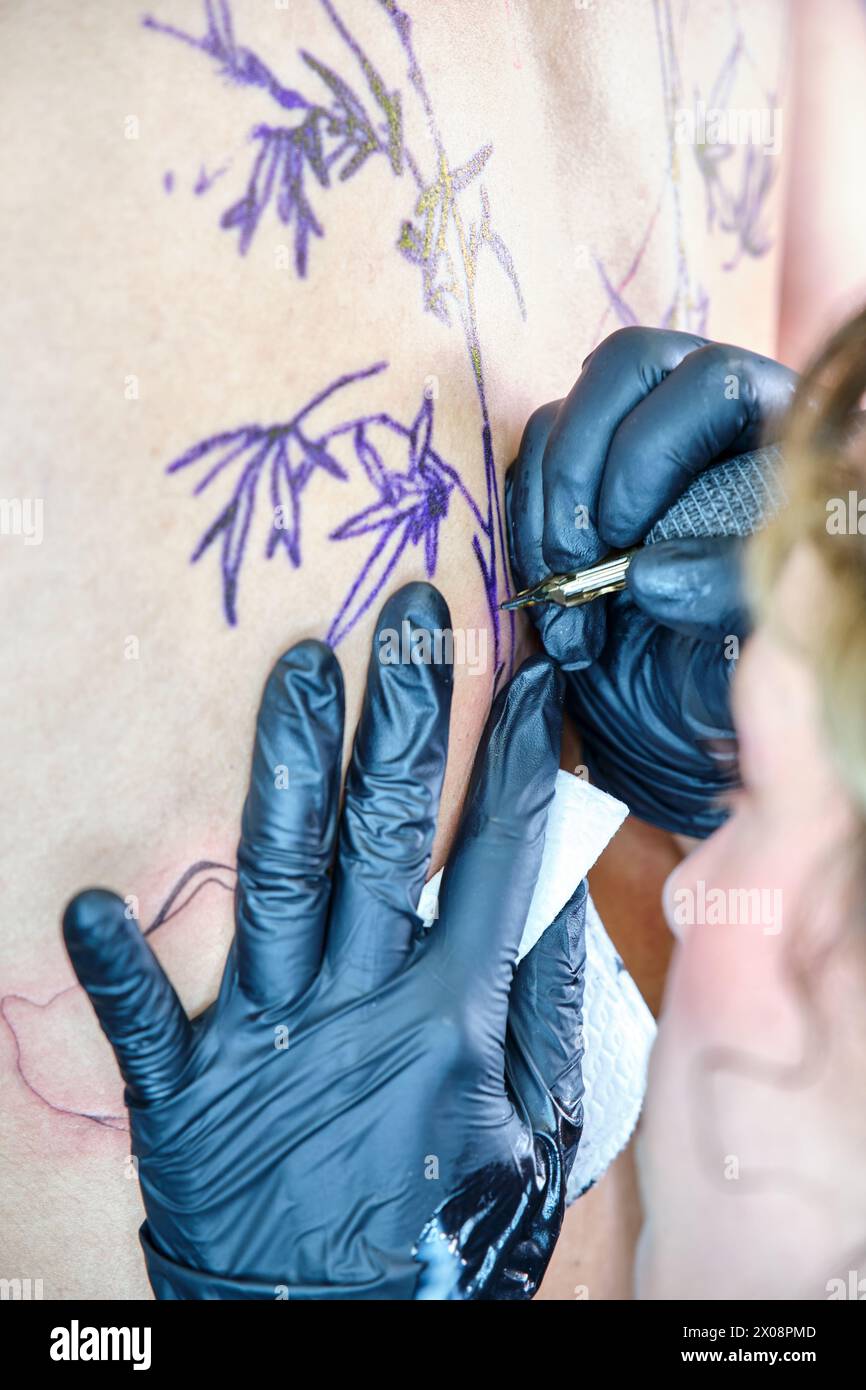 Vista ravvicinata di una donna irriconoscibile che tatua un disegno sulla pelle di un cliente in uno studio di tatuaggio pulito. Foto Stock