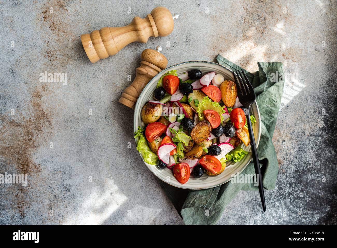 Vista dall'alto di una rustica insalata di patate mediterranee con patate primaverili, olive nere, pomodori ciliegini, cipolle primaverili, lattuga croccante, e i radiaci, servono Foto Stock