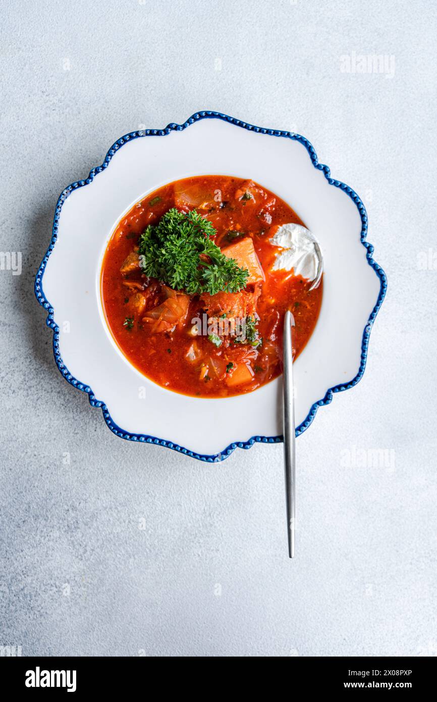 Saporita zuppa di borscht ucraino preparata con barbabietola, carne tenera e servita con un cucchiaio di panna acida, guarnita con prezzemolo Foto Stock