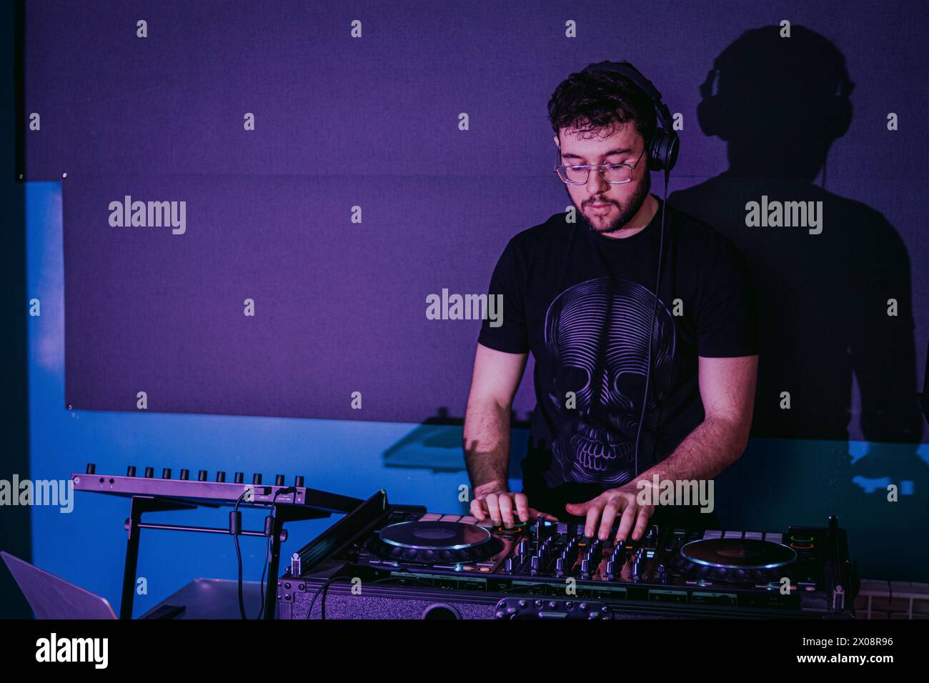DJ maschile concentrato che mixa brani su giradischi con una silhouette ombrosa sullo sfondo di un club Foto Stock