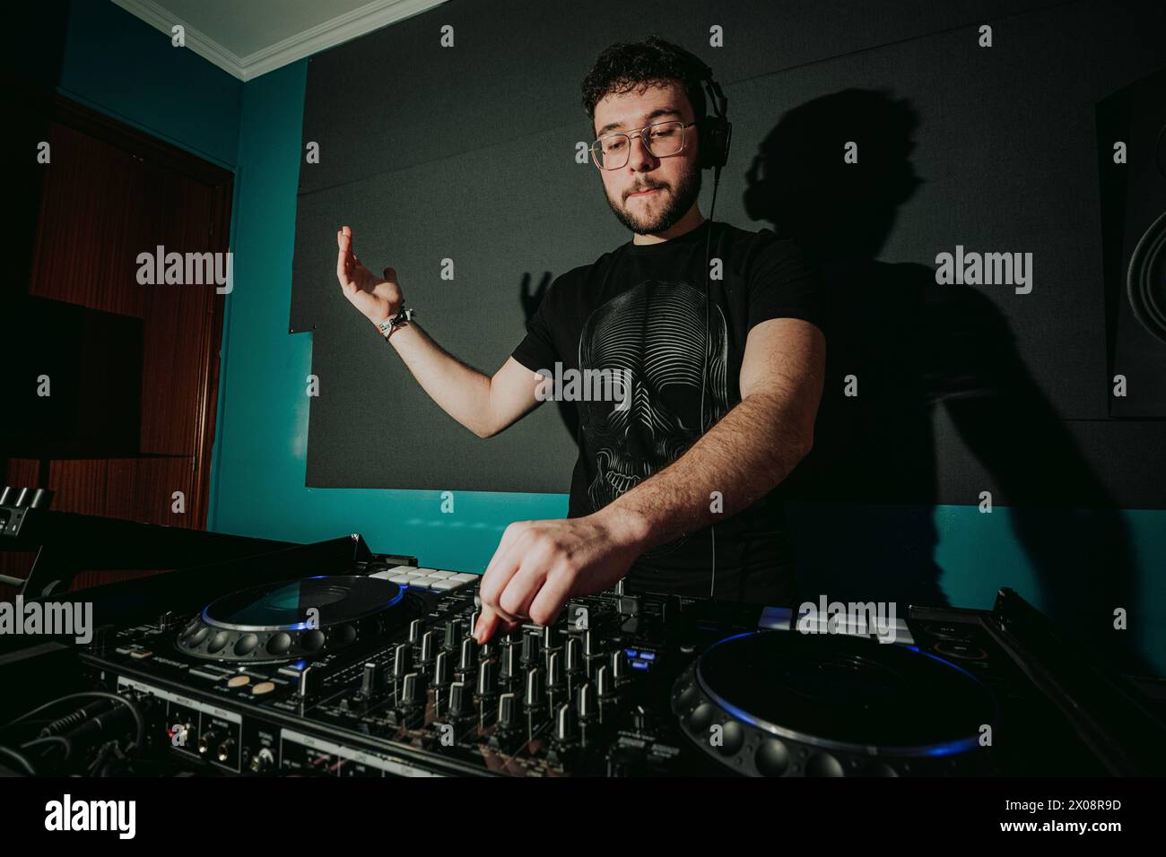 Un DJ maschile mescola brani su un mixer audio professionale in una sala studio buia con illuminazione blu Foto Stock