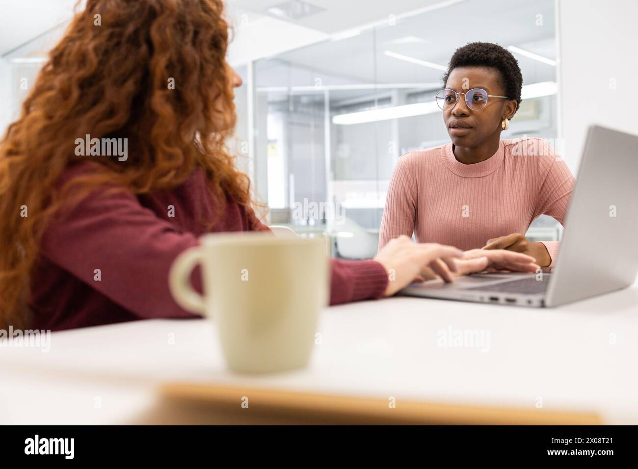 Due donne professionali si impegnano in una discussione in uno spazio di lavoro, con una donna afroamericana che ascolta attentamente il suo collega. Foto Stock