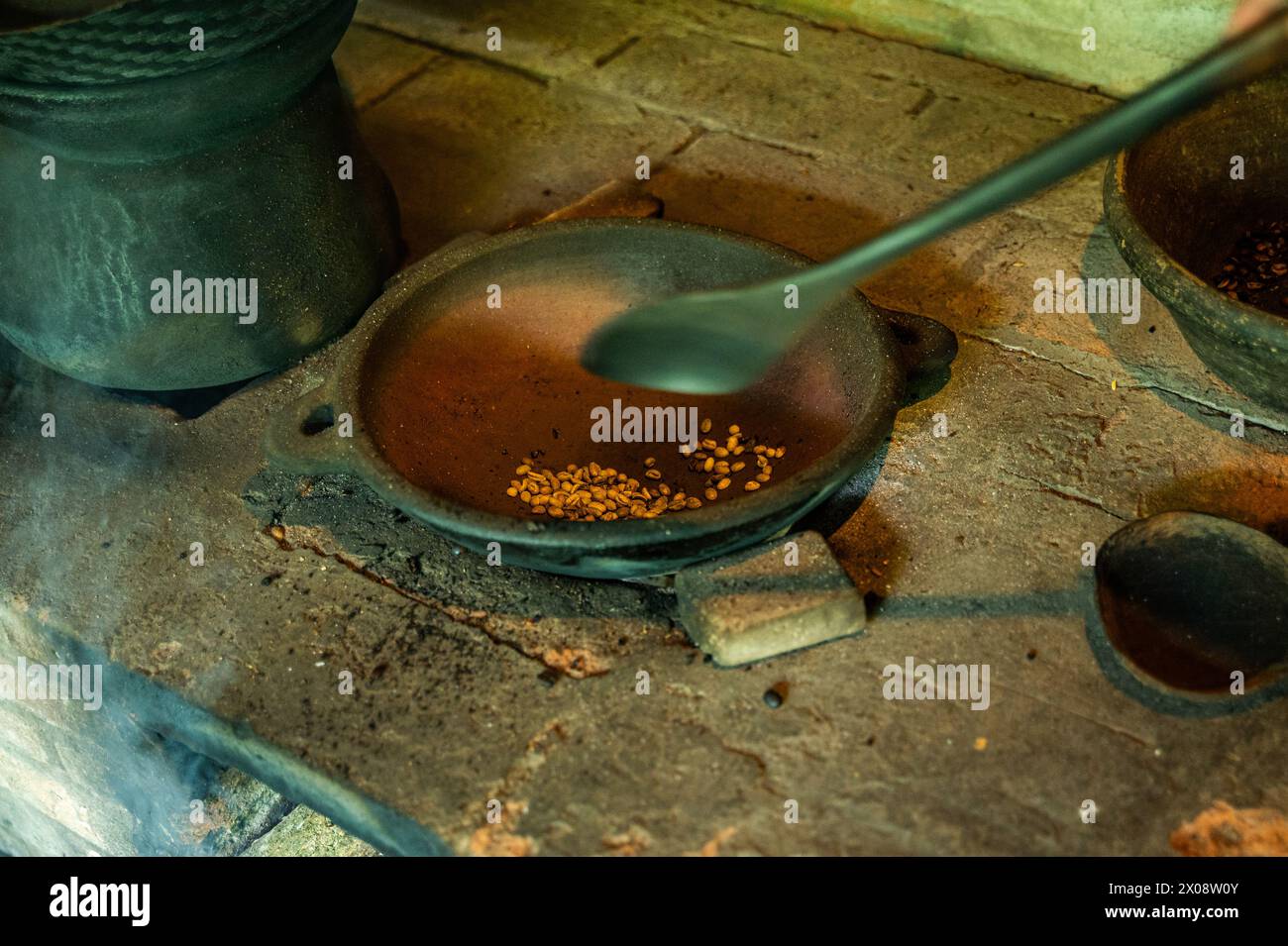 Un primo piano di chicchi di caffè appena tostati in una tradizionale pentola di argilla sopra una stufa a legna, catturando l'essenza dell'autentico caffè balinese. Foto Stock