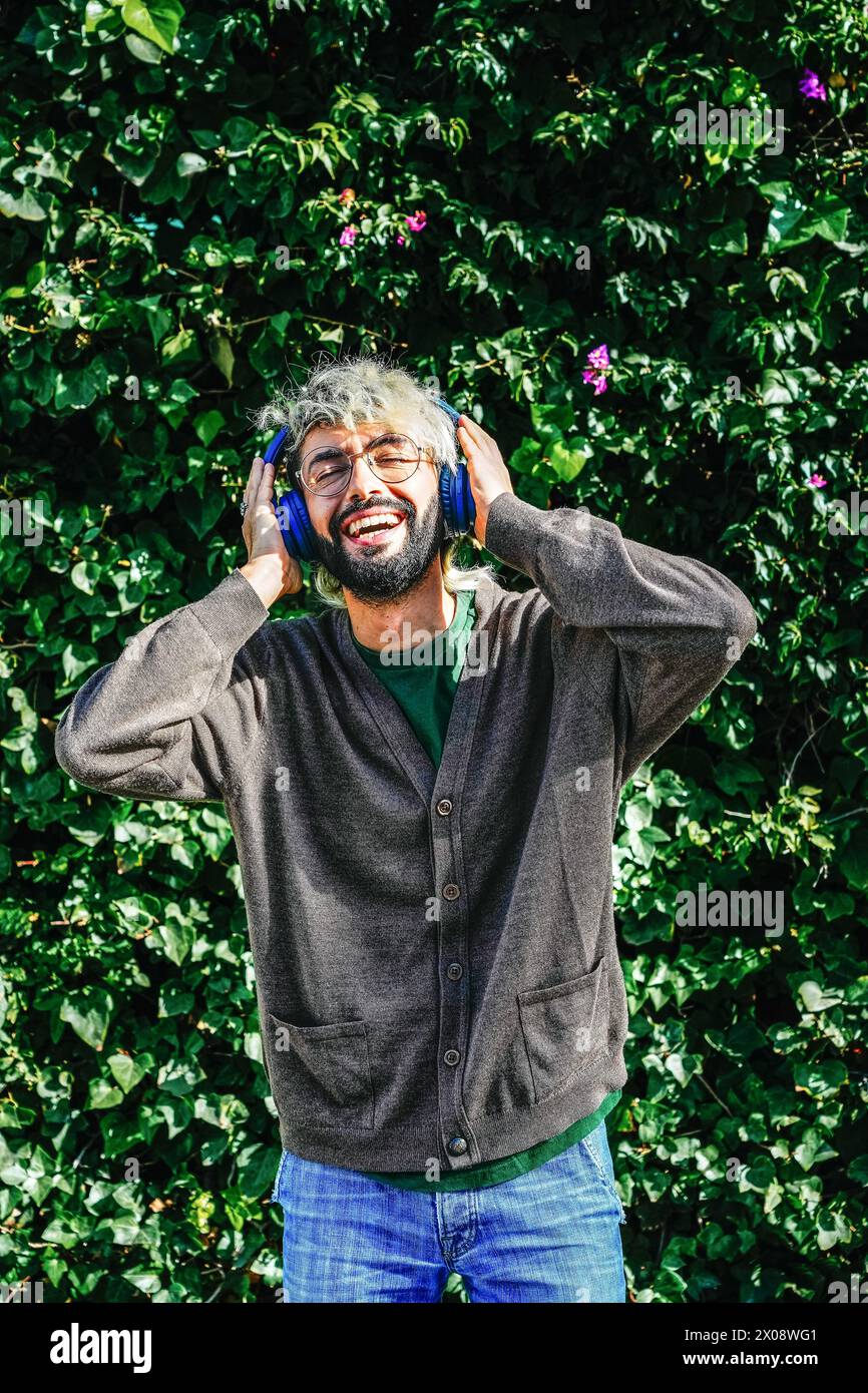 Un uomo che emette un fascio di luce gode di un momento euforico con le cuffie indossate, su uno sfondo lussureggiante di edera verde e fiori Foto Stock
