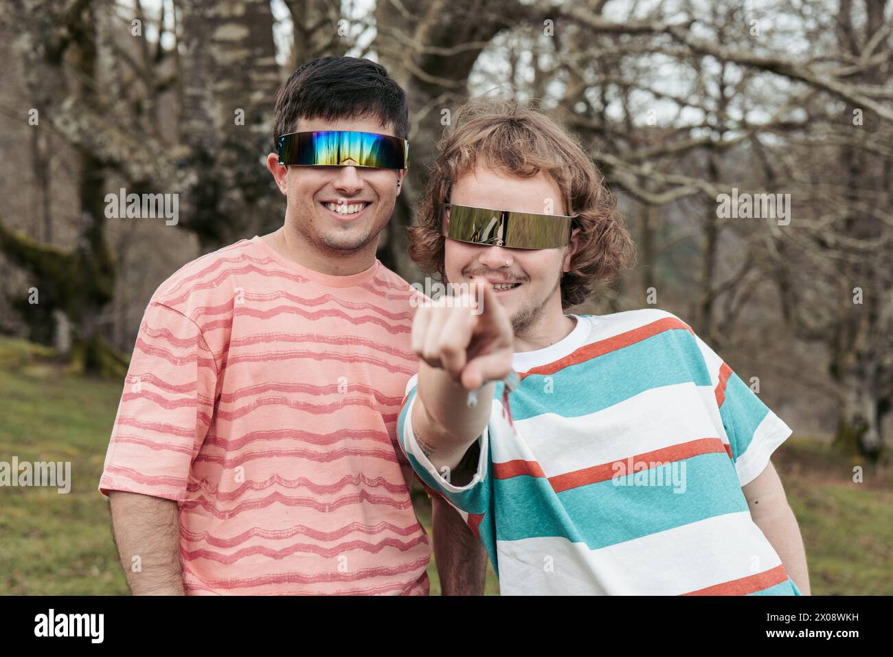 Una coppia allegra si impegna giocosamente con la fotocamera, con occhiali da sole riflettenti e sorrisi luminosi in un parco idilliaco Foto Stock
