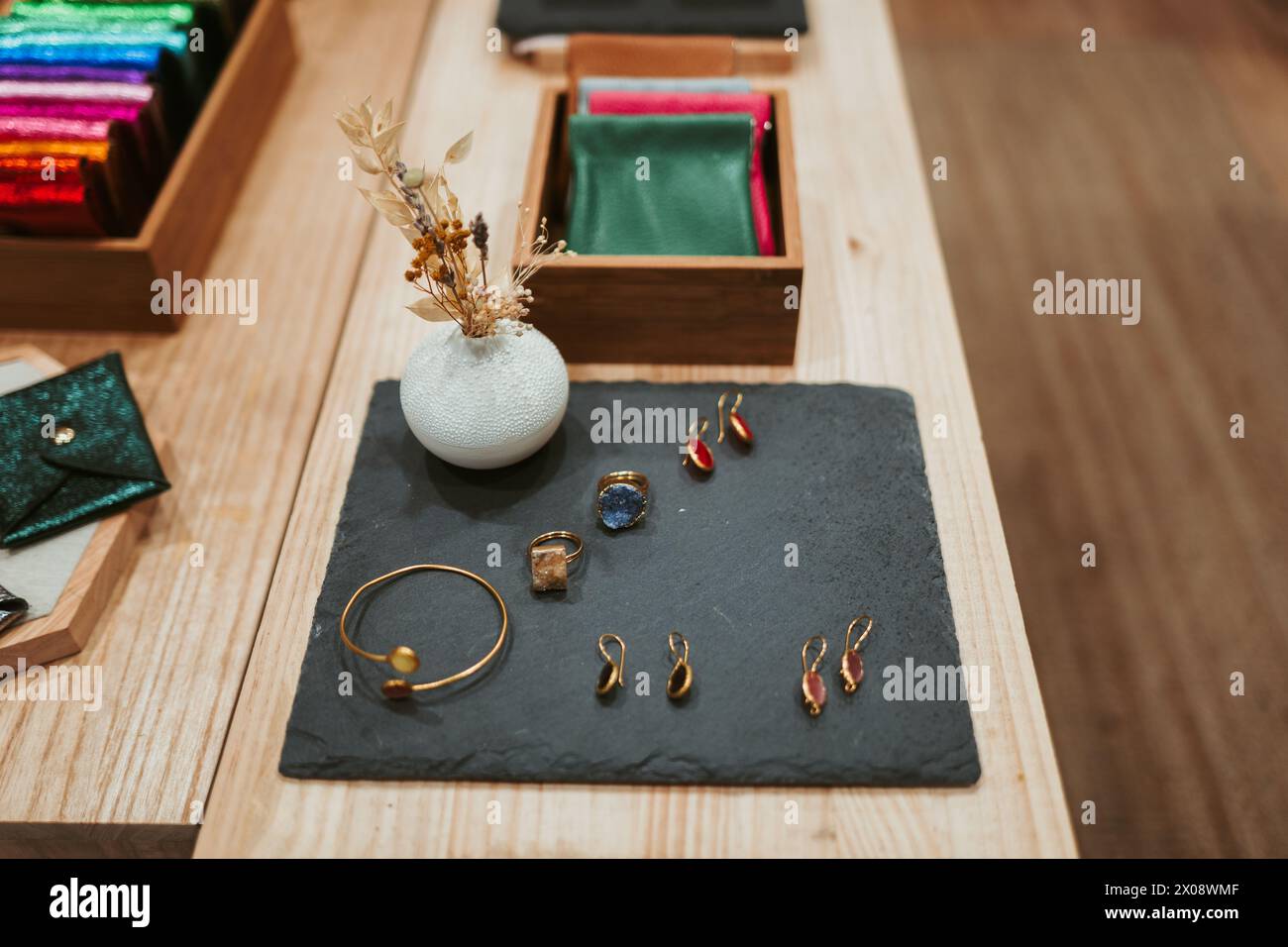 Una selezione curata di raffinati gioielli presentati elegantemente su uno sfondo di ardesia in un ambiente boutique con accenti in legno e fiori secchi Foto Stock