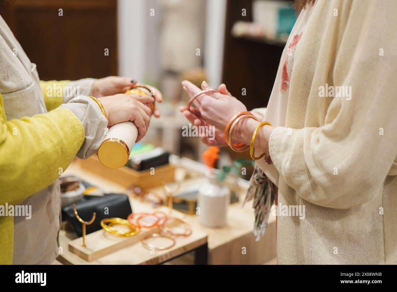 Due donne mettono alla prova la vestibilità dei braccialetti colorati in una boutique, mostrando il loro stile alla moda primaverile Foto Stock