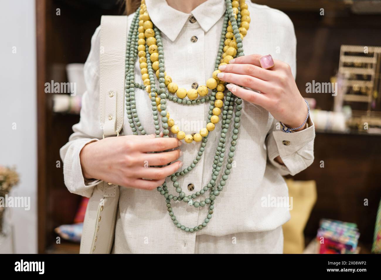 Donna elegante con collane con perline a strati in tonalità primaverili, che toccano con eleganza gli accessori con mani curate Foto Stock