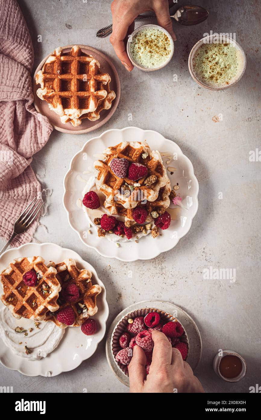 Un ambiente accogliente da forno con waffle ricoperti di lamponi e panna, oltre a tazze di latte matcha Foto Stock