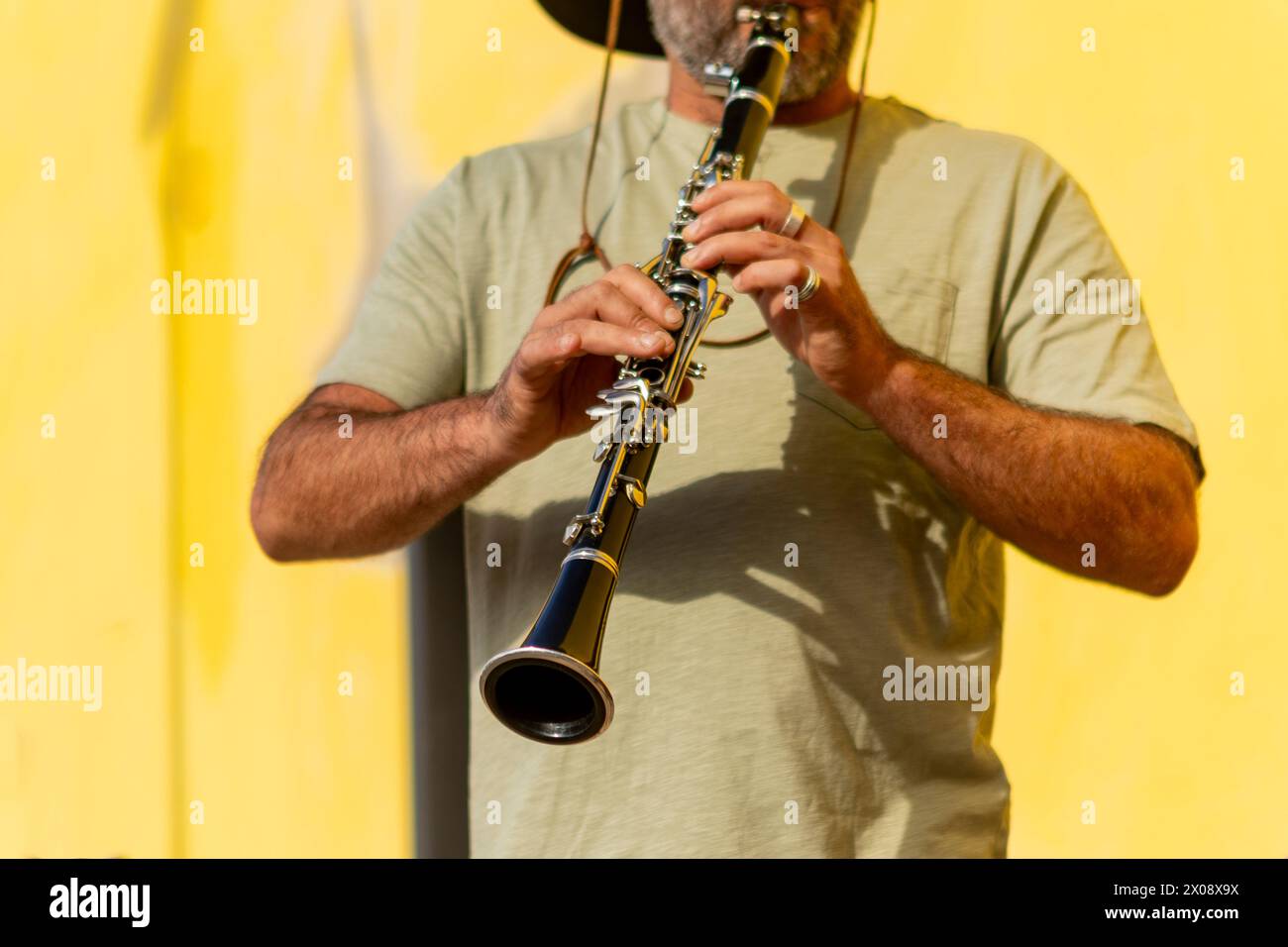 Musicista di strada corta e irriconoscibile che suona sapientemente il clarinetto, con un vivace sfondo giallo che accentua la performance. Foto Stock