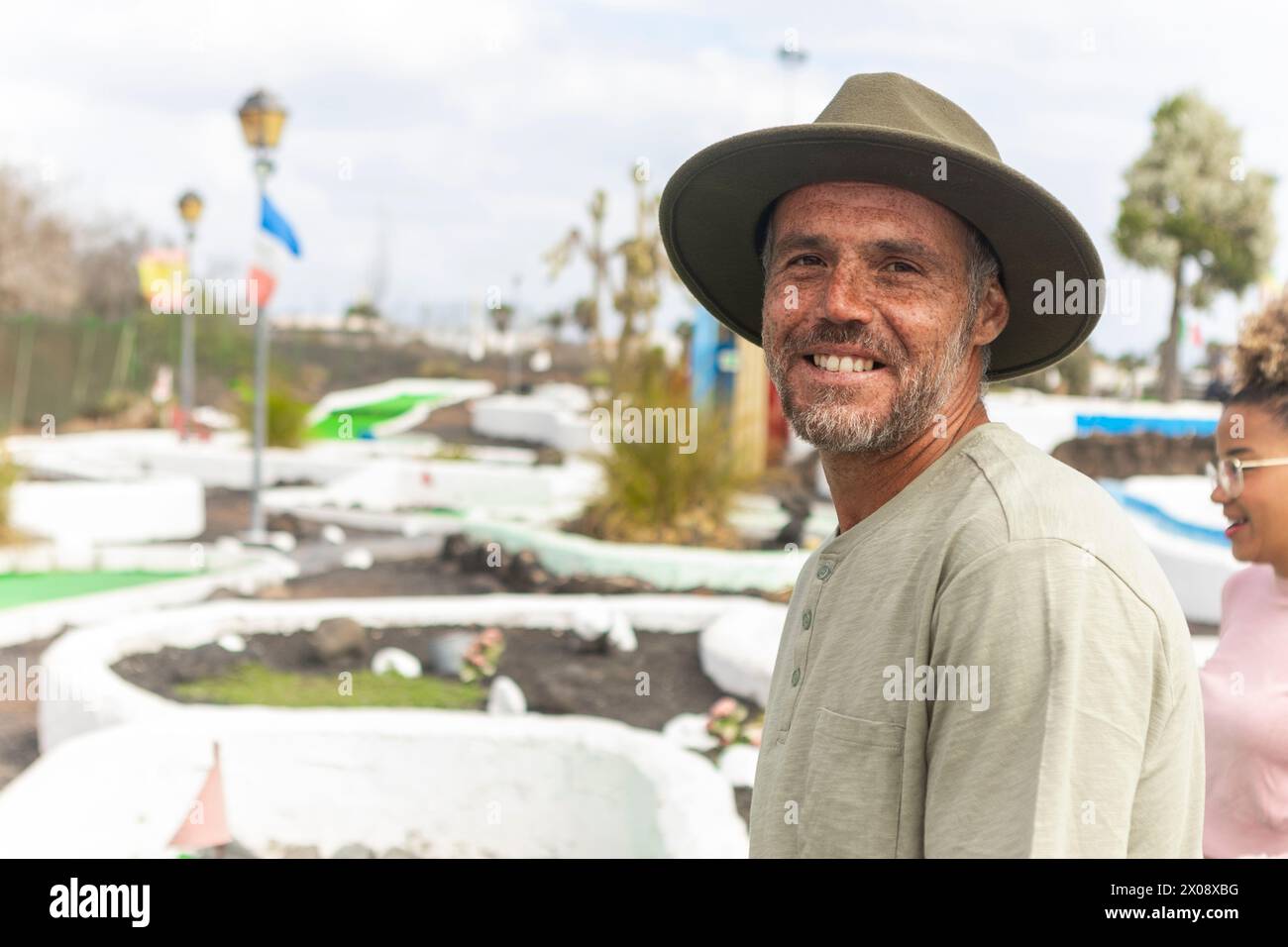 L'uomo sorridente ama una giornata di sole al campo da minigolf con gli amici sullo sfondo. Foto Stock