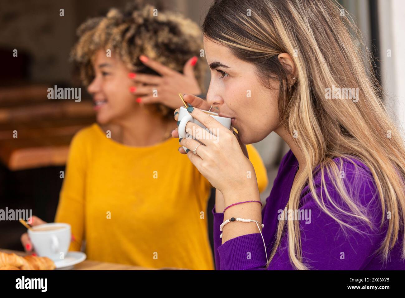 Due amici si impegnano in una vivace chiacchierata con un caffè in un accogliente ambiente da caffè, con uno che sorseggia una bevanda Foto Stock